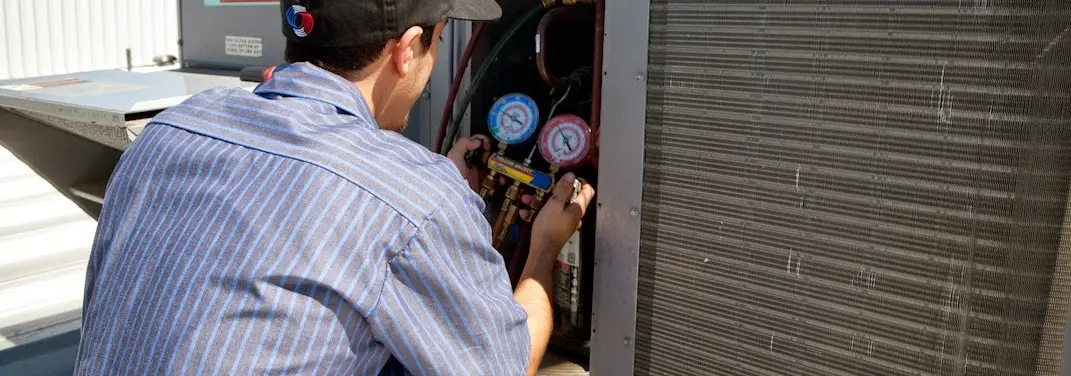 HVAC technician servicing a condenser unit in Tiverton